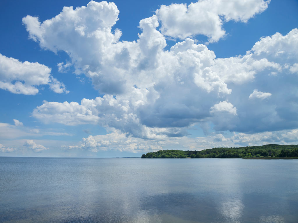 A photo of Mille Lacs Lake in Minnesota, with calm waters, partially cloudy skies and the shoreline visible to the right of the photo.