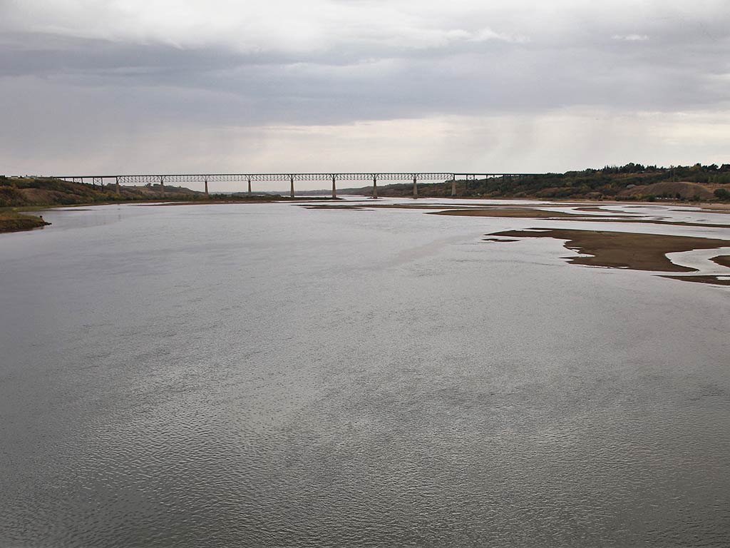 A view accross the calm waters of Diefenbaker Lake in Saskatchewan, looking towards a bridsge in the distance on a cloudy day