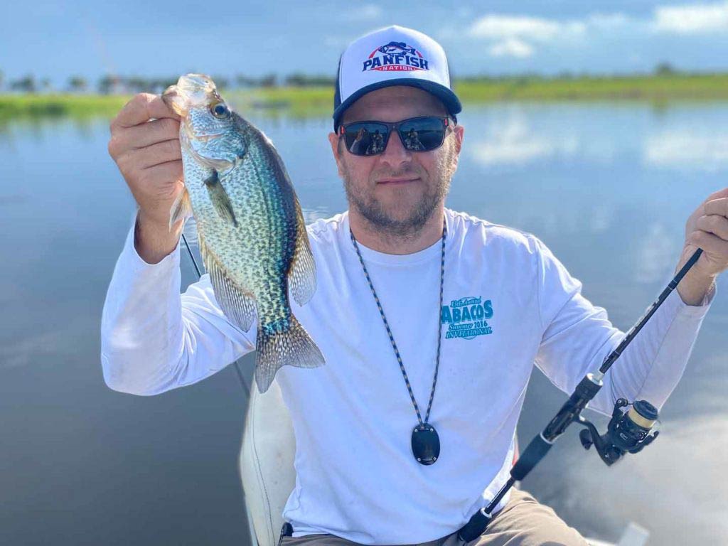 A man holding a rod in one hand and a Crappie in the other hand on a boat fishing on a lake in Texas