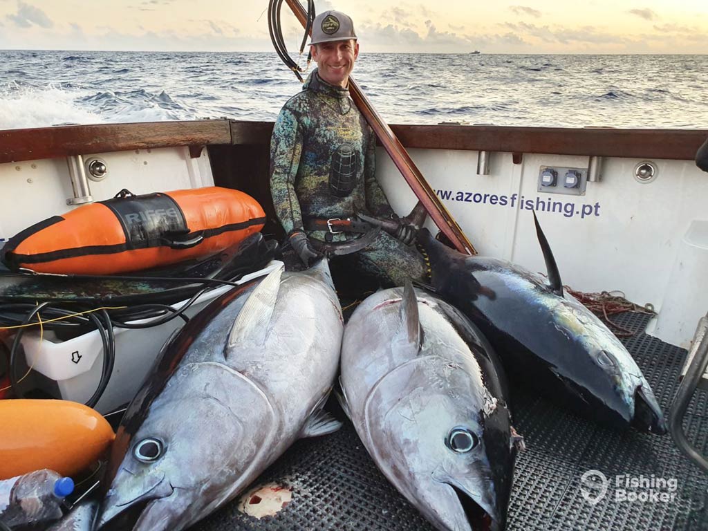 A photo featuring a proud angler while squatting on a charter fishing boat and posing with three big Bluefin Tuna on the floor in front of him