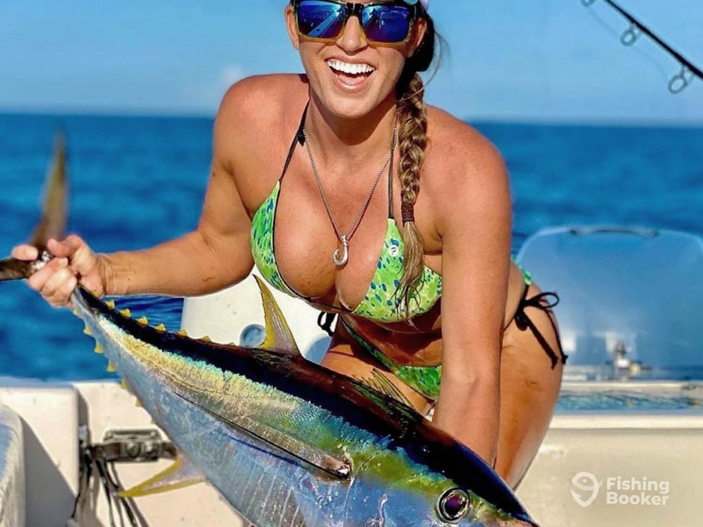A photo of a female angler wearing a pair of sunglasses and smiling while posing with Yellowfin Tuna caught in Mexico during the high season