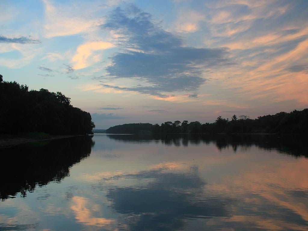 A view down the Illinois River near sunset on a cloudy day, with green trees visible on either side of the river on its banks