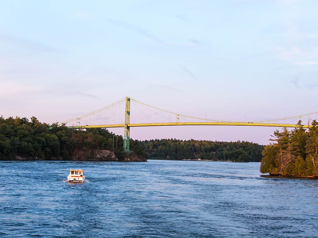 An aerial view looking down the St. Lawrence River in New York, with a boat visible on the water heading towards a large bridge