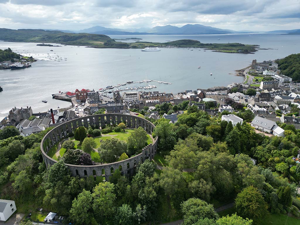 An aerial view looking down on the town of Oban in Scotland and the sea on a cloudy day, with an amphitheater visible in the foreground