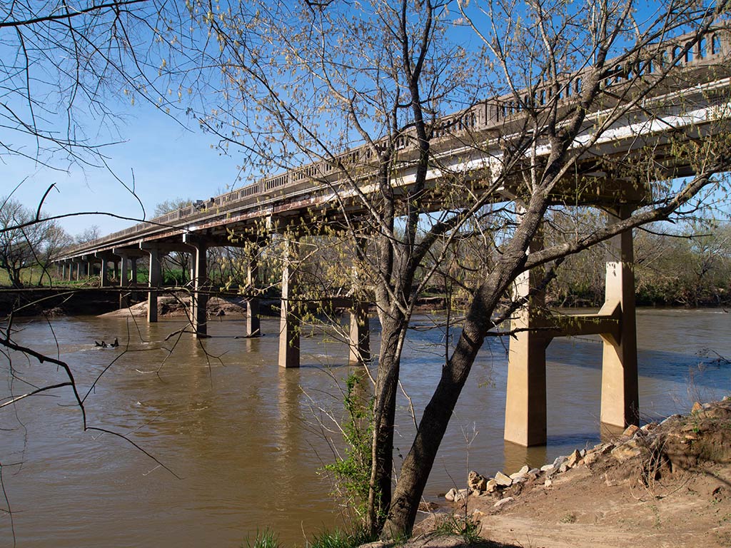 A view of the Yadkin River flowing under a bridge in North Carolina on a clear winter's day, with a barren tree visible in the foreground