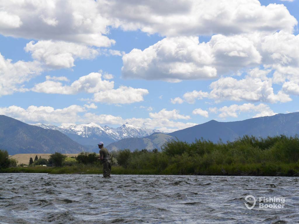 A beautiful view of a fly fishing angler standing the river and casting while posing against the magnificent greenery and mountains