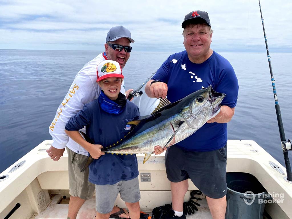 A photo featuring a kid and two adult anglers standing on a charter fishing boat and posing with Tuna they caught while deep sea angling in San Diego