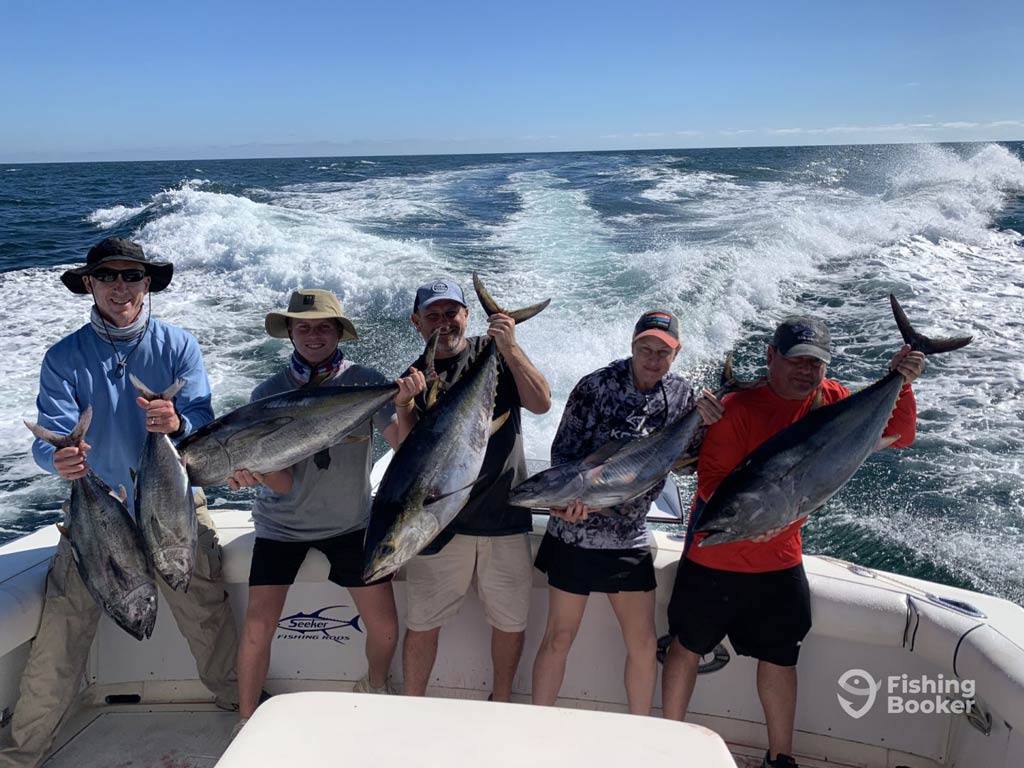 A photo featuring five anglers standing on a charter boat while it’s moving far offshore and posing with a catch each; one of the anglers holds two smaller fish in his hands
