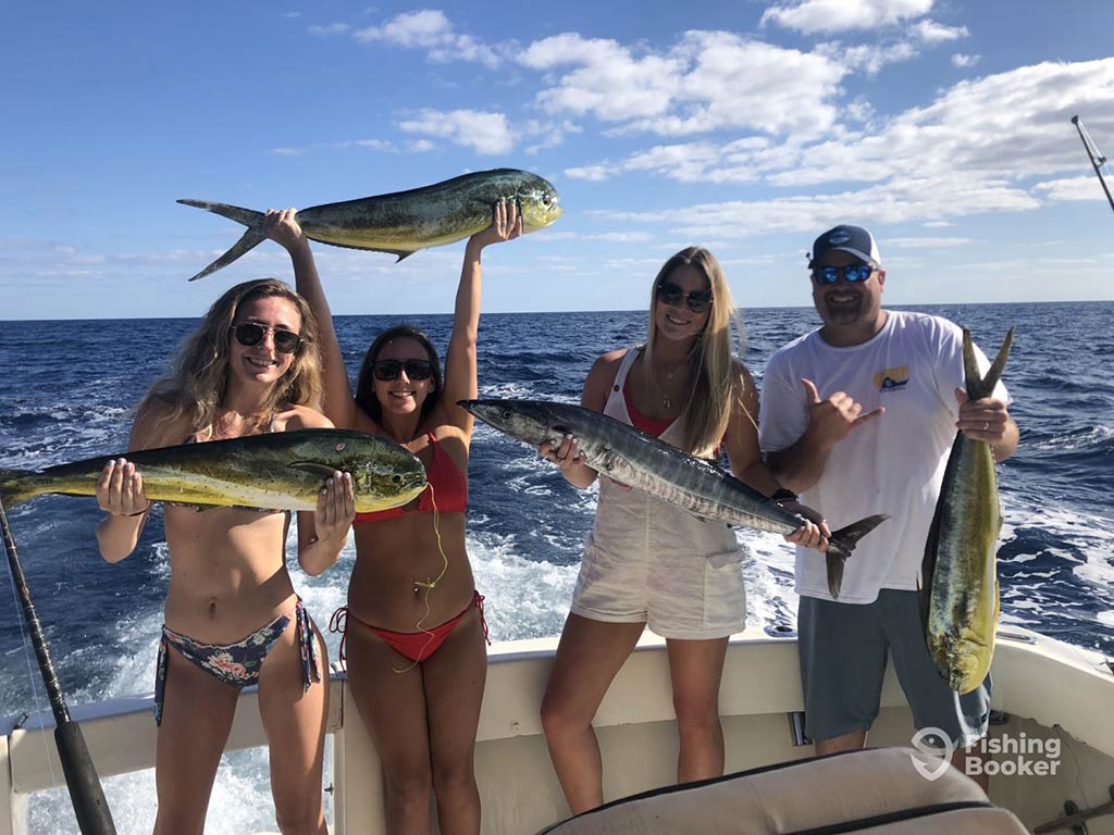 A group of three women and a man standing aboard a fishing charter in the Bahamas on a sunny day and showing off their catch of different Mahi Mahi and Wahoo
