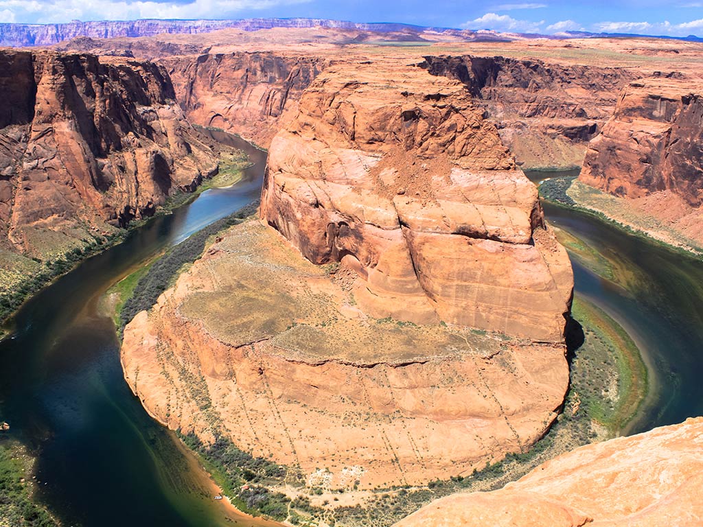 An aerial view of a river winding its way around a large orange-rocked canyon in Arizona on a clear day