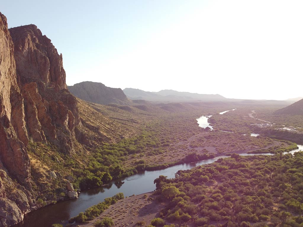 An aerial view looking down to a stream near Sedona, AZ, on a clear day with a large rock visible on the left of the image and the sun visible in the distance