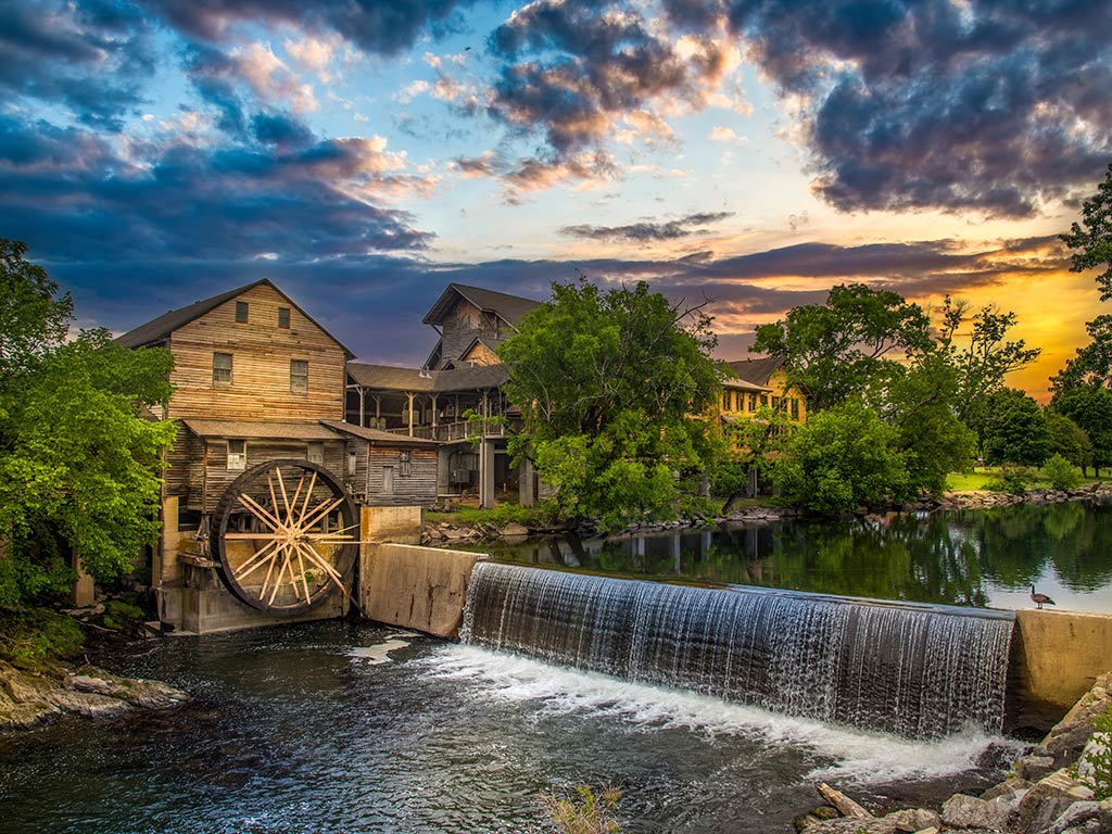 A view across a man-made waterfall or weir towards a mill in Gatlinburg, TN at sunset on a cloudy day