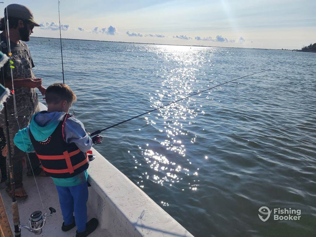 A young boy fishing over the side of a boat in the ocean on a clear day
