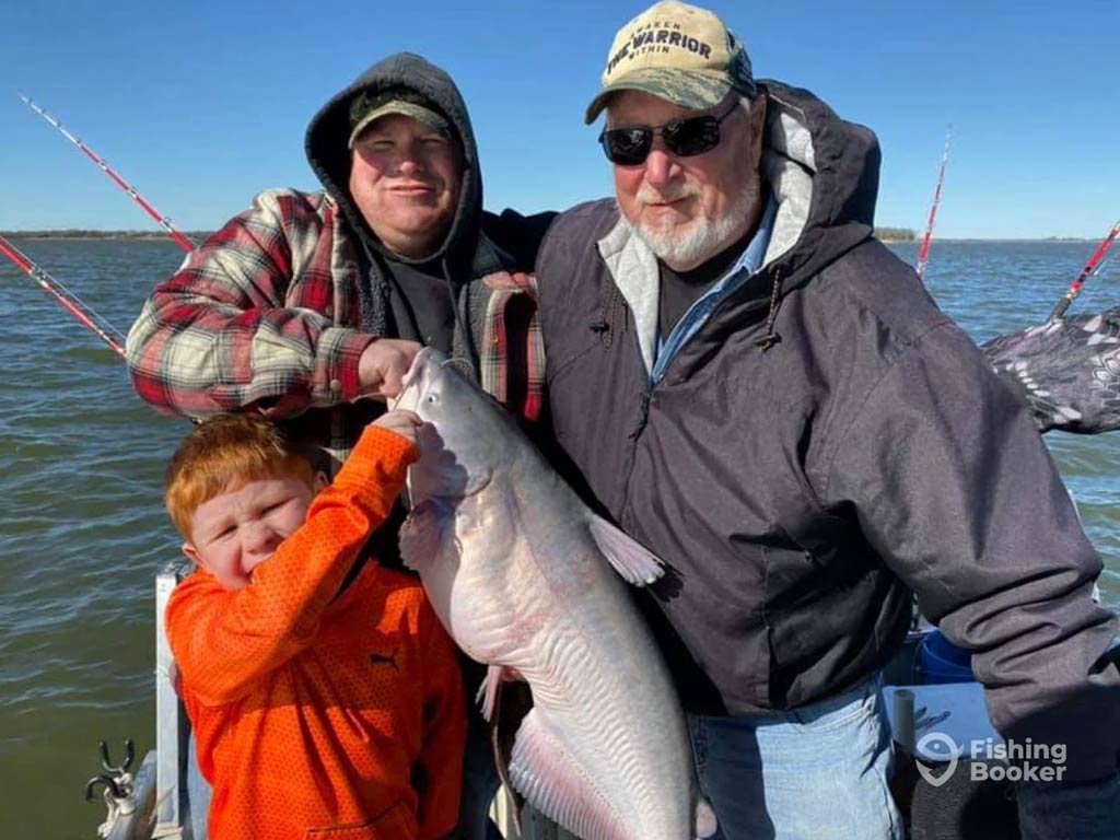 A photo featuring three anglers, two adults and a child, standing on a charter boat and posing with a decent-sized Blue Catfish caught in Texas with F.L. Catfish Fishing Guide