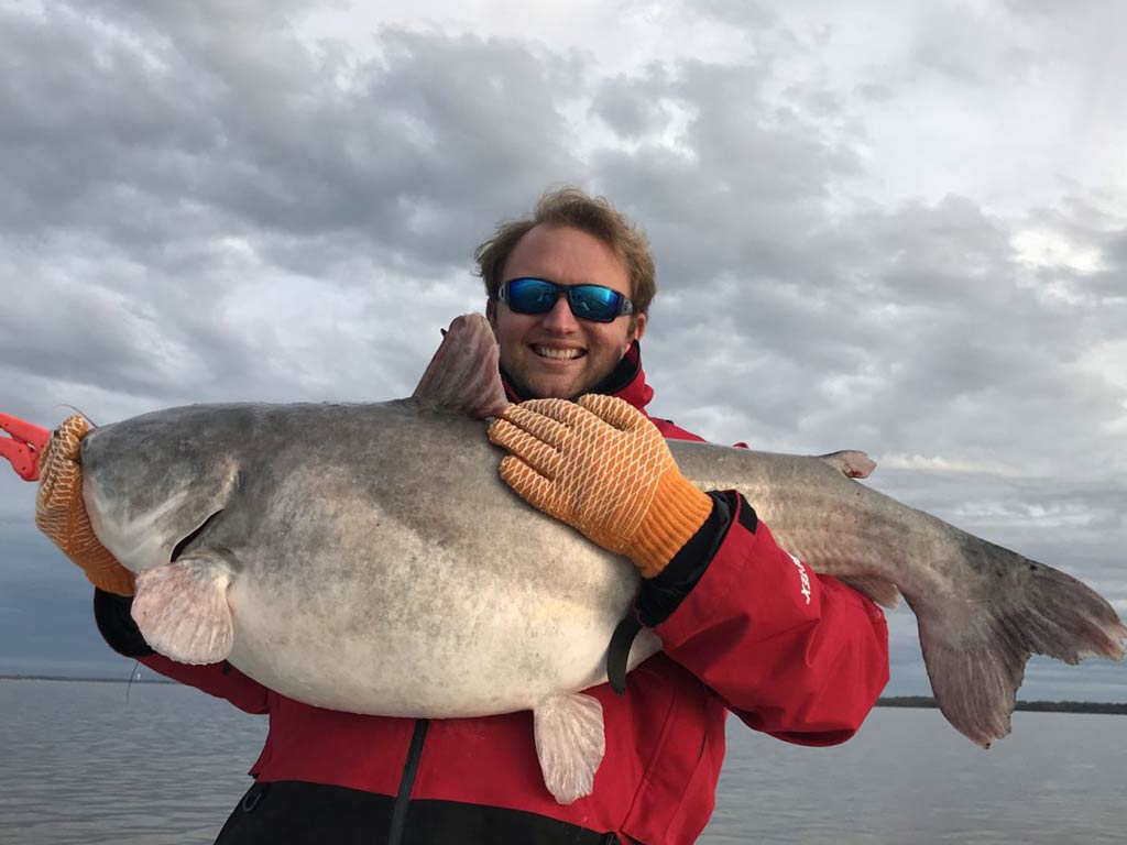 A photo of an angler proudly posing with a huge Blue while standing on a charter boat during the winter angling season and a cold and cloudy day out on the water