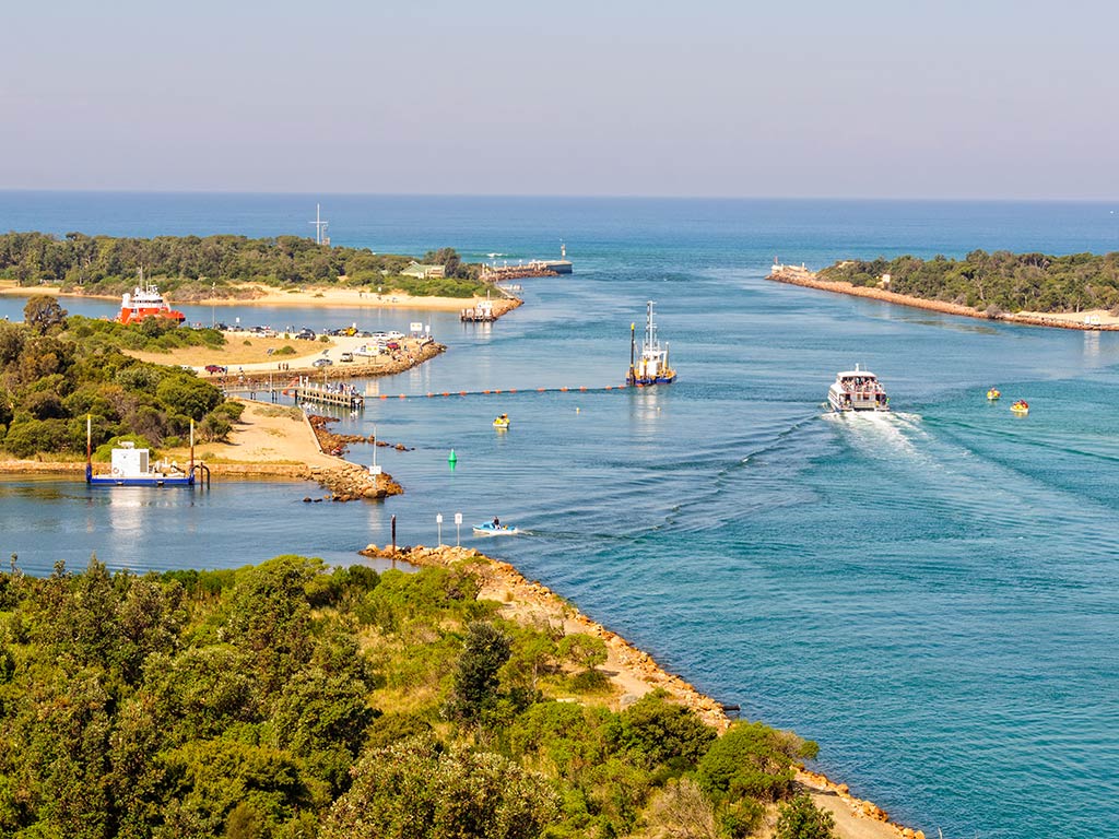 A view out through an inlet from the Gippsland Lakes towards the ocean, with plenty of boat traffic visible on a clear day