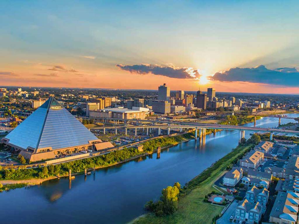 An aerial view of Memphis, Tennessee, with the Pyramid, Mississippi River, a bridge over it, and downtown photographed at sunset.