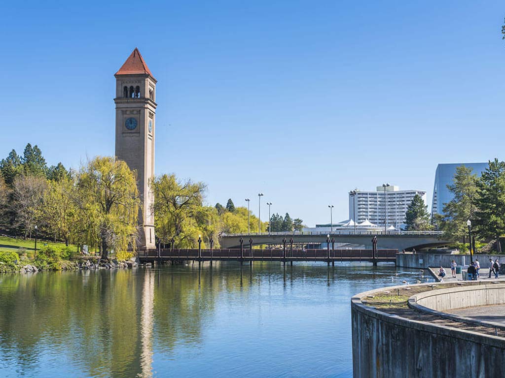 The Spokane River flowing through the center of Spokane, one of the best fishing cities in the US, with a clock tower rising through the trees on the left.