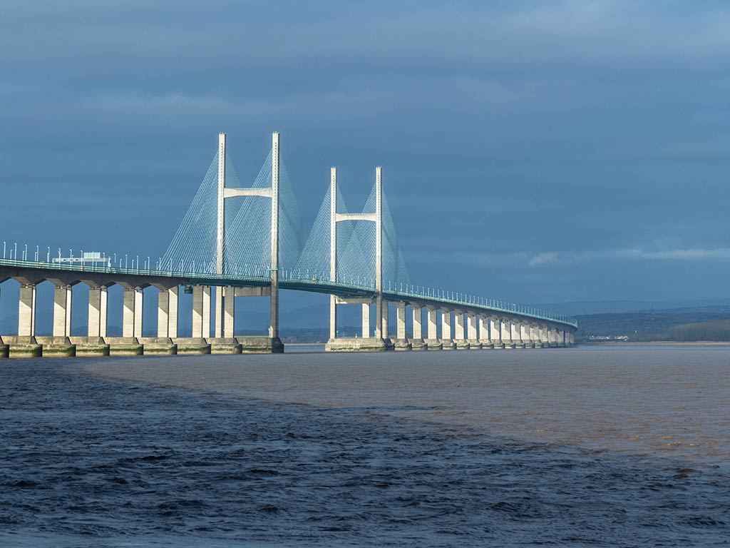 A view across the waters of the Bristol Channel with the Second Severn Crossing bridge visible, dominating the view beween Wales an England on a cloudy day