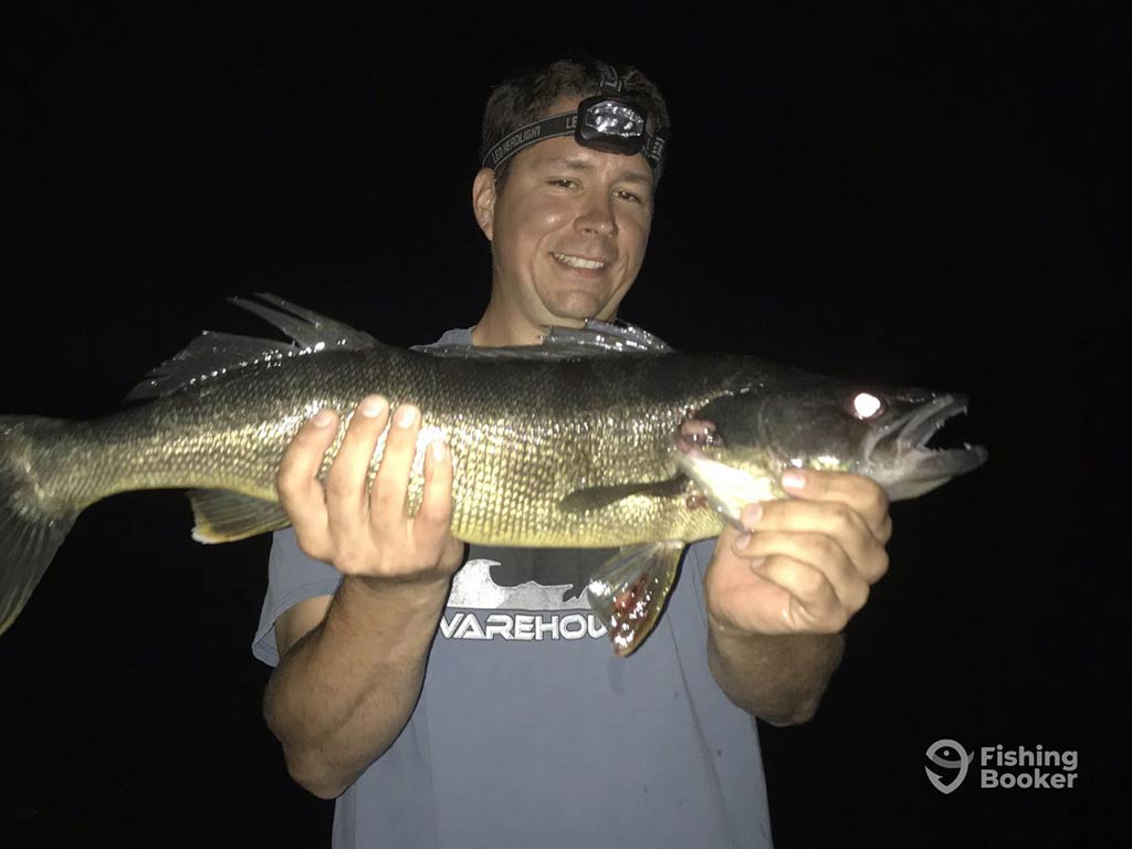 A man wearing a headlamp holding a Walleye at night with a black background behind him