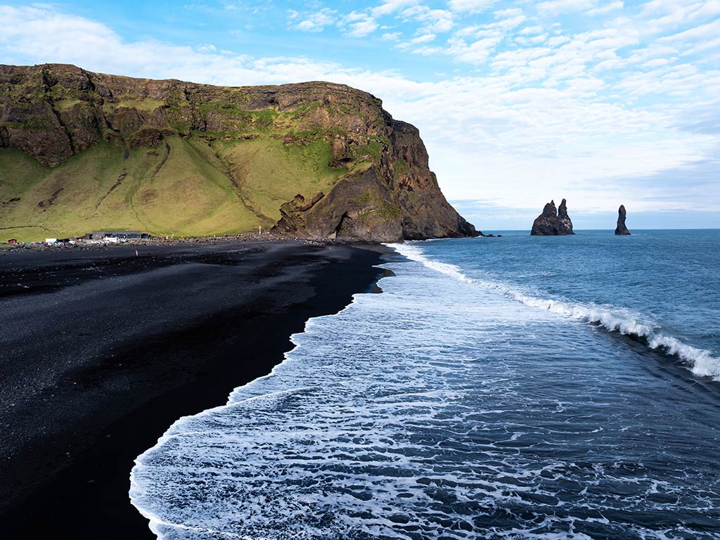 A scenic black sand beach with ocean waves crashing into it on the south coast of Iceland on a clear day