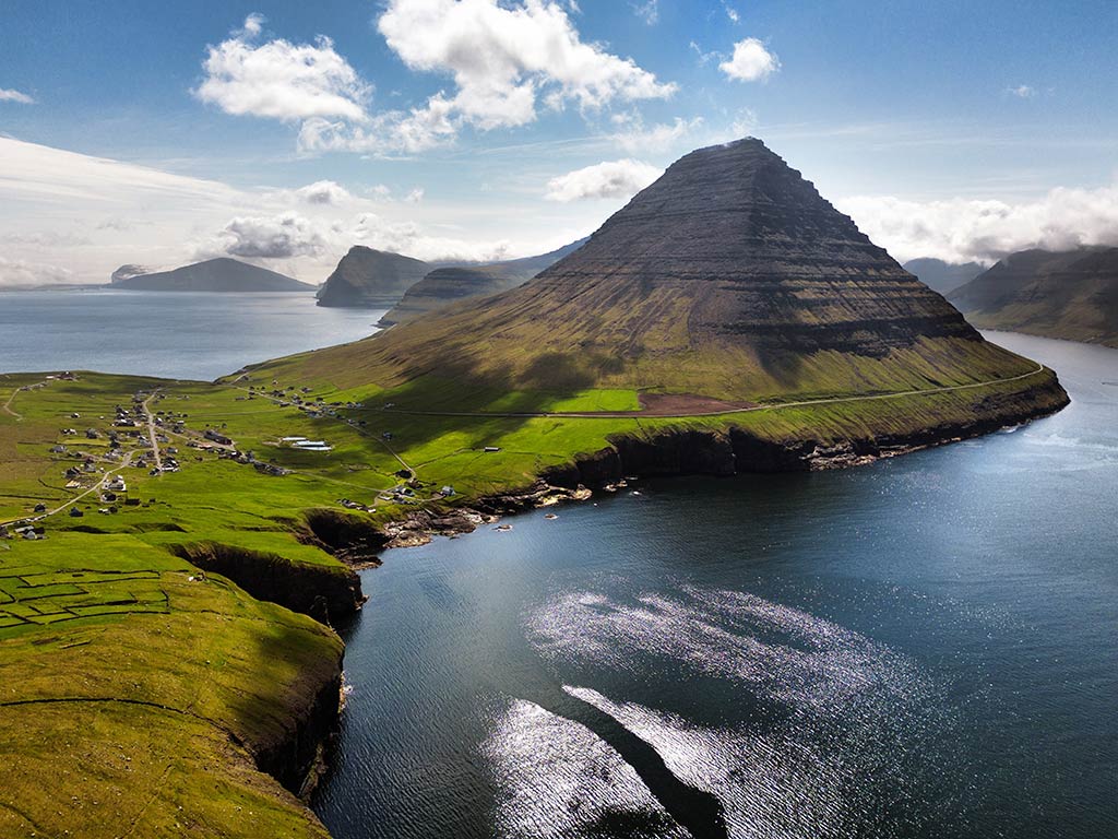 A scenic mountain landscape next to a calm bay in the Faroe Islands on a day with sunny intervals