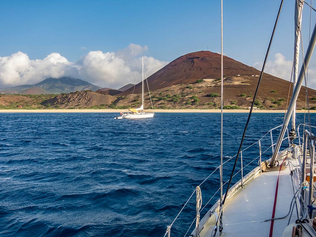 A view from a boat towards the shores of the remote Ascension Island in the Atlantic Ocean with another boat visible in front of the shoreline on a clear day
