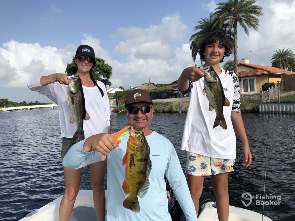 Sure, here's a revised version of the description:
Three people on a boat hold up their catches, each displaying a fish. They're wearing casual outdoor clothing. The water and palm trees are visible in the background.