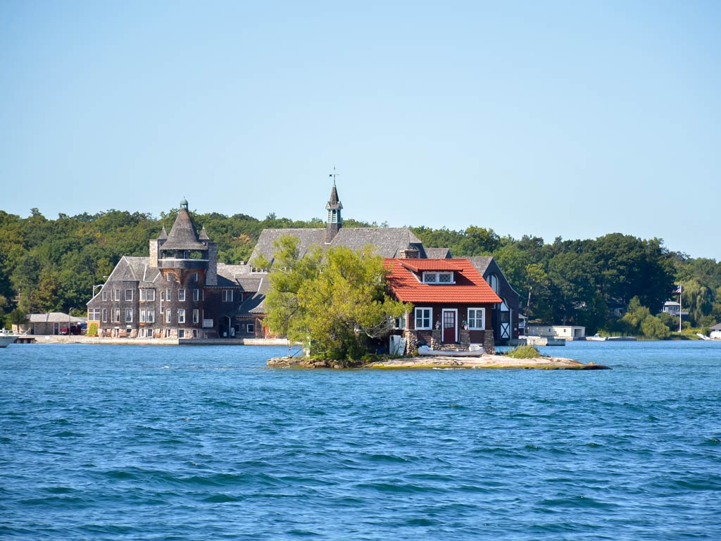 A view of a small red-roofed house and larger buildings in Kingston, all surrounded by water, making it ideal for fishing enthusiasts. Lush trees stand under a clear blue sky. 