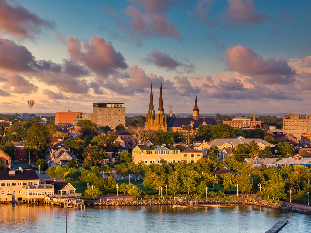 A scenic view of Charlottetown with historic buildings, water, and a hot air balloon drifting in the sky under a cloudy sunset paints an idyllic picture. The charm of the old architecture captures the town's rich history, while the gentle flow of the river invites anglers to try their luck with trophy catches.