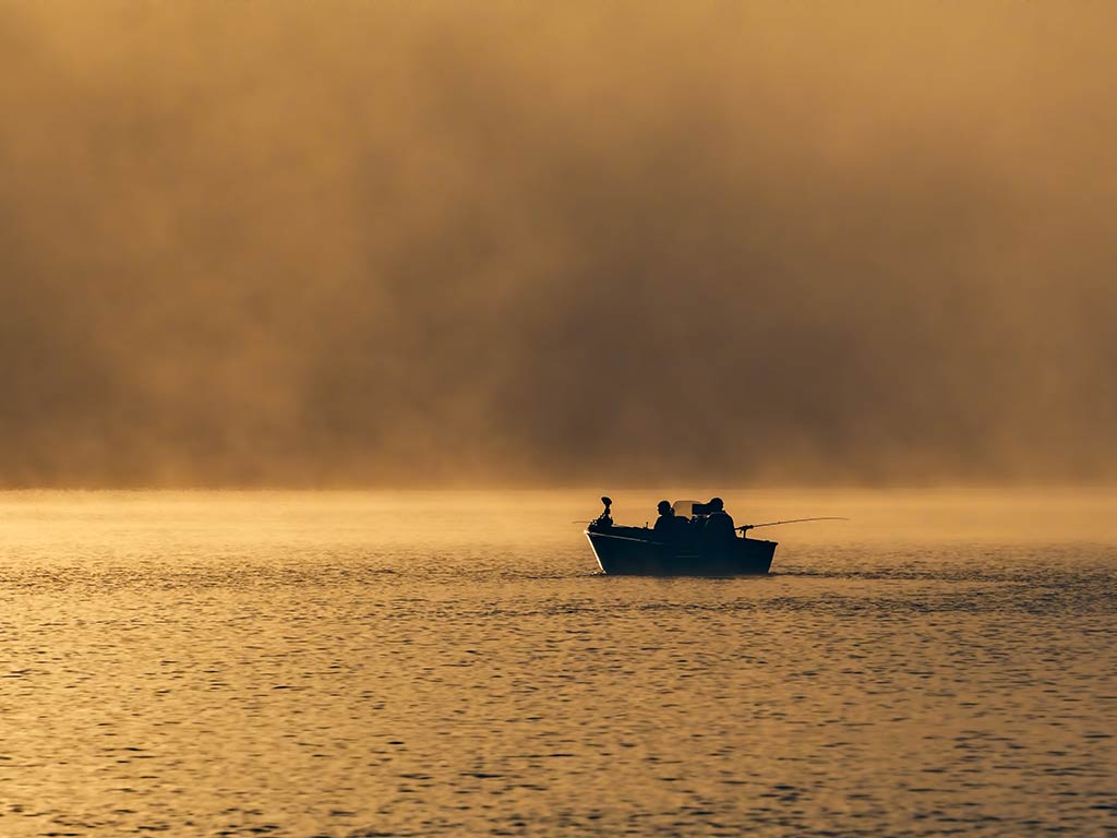 A view across a lake near sunset with a lone boat set up for fishing