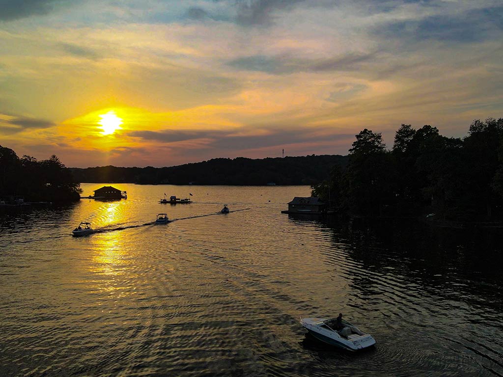 An aerial view of Lake Hopatcong looking towards the sun setting beyond some boats on a clear day