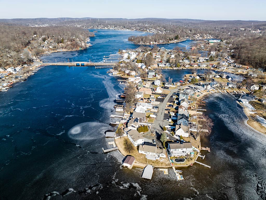 An aerial view of a frozen Lake Hopatcong on a clear day with a town visible in the foreground and a bridge visible on the left of the image