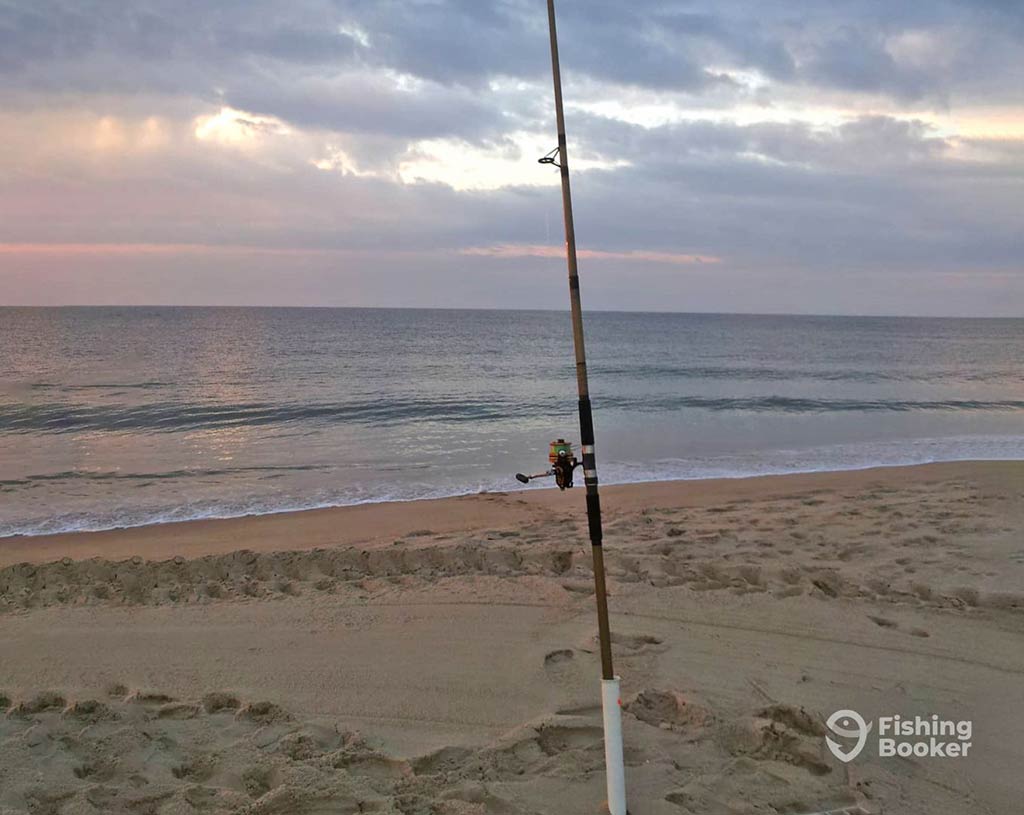 A fishing rod standing in the sand on Assateague Island's calm beach at sunset, with gentle waves whispering in the background.
