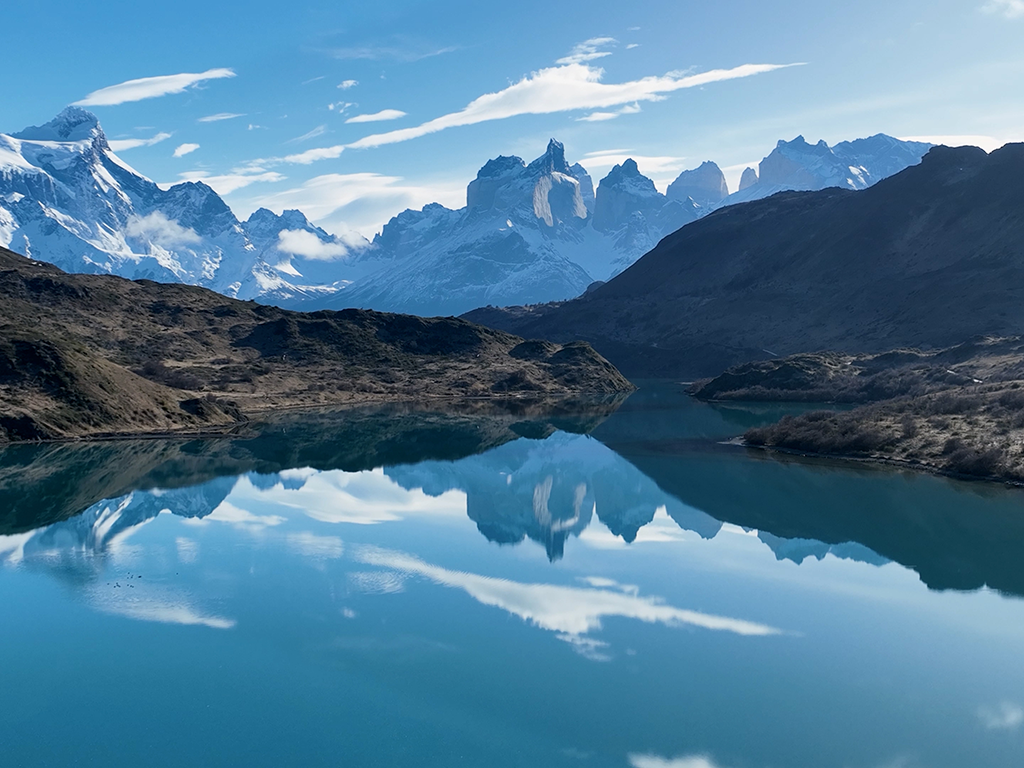 A mountain range is reflected in a calm blue lake under a clear sky somewhere in Chile.