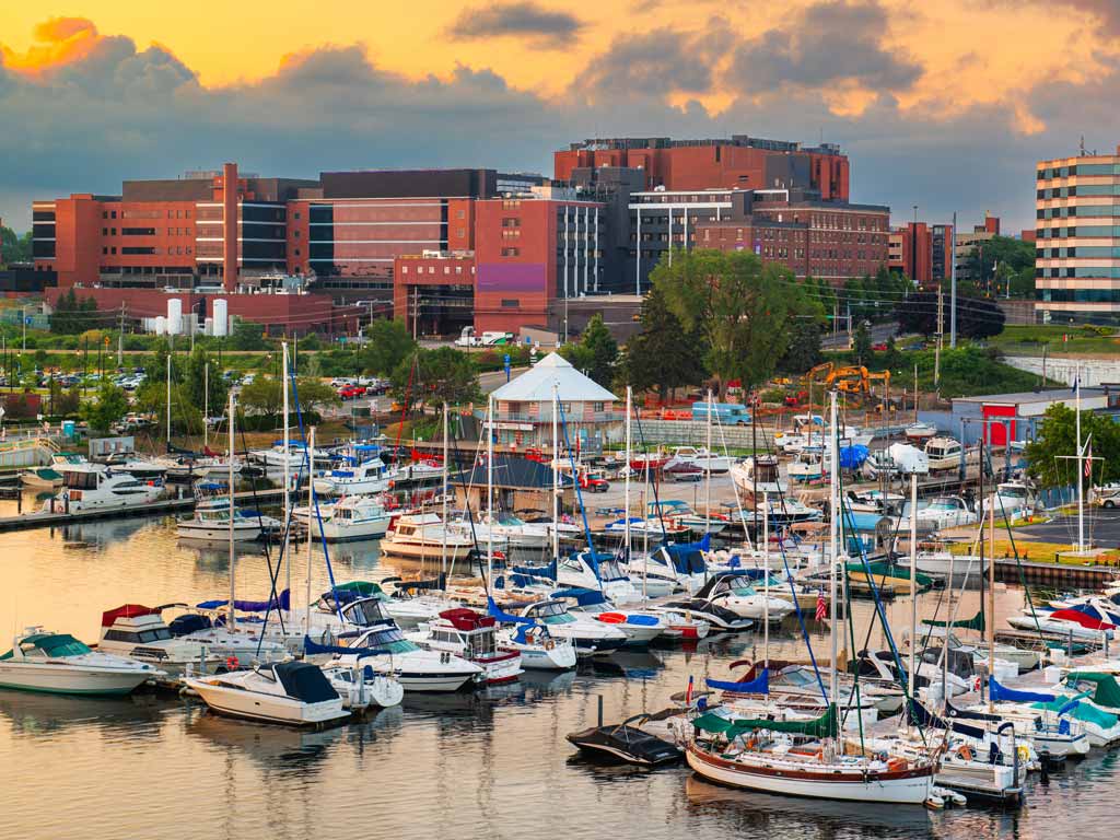 A view of Erie, PA, one of the top Memorial Day fishing destinations, with a marina filled with docked boats sitting in the foreground, and brick red buildings in the background.