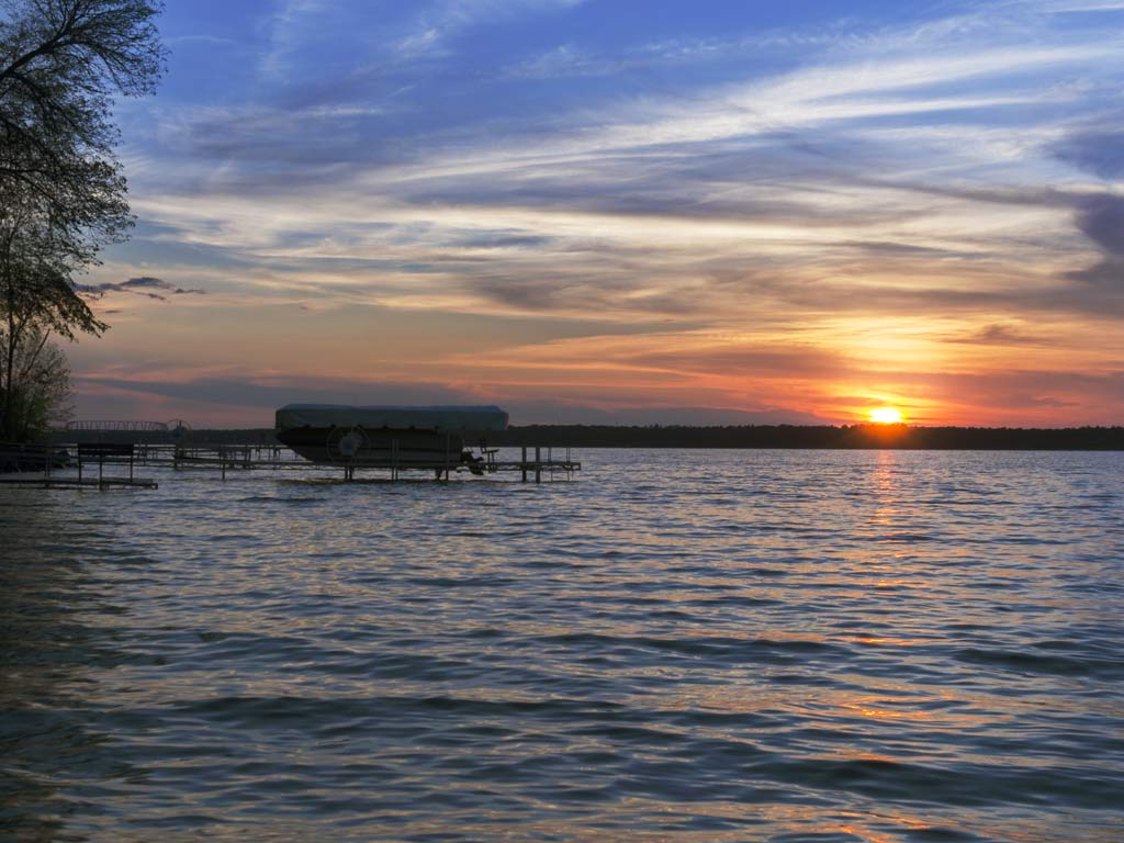 A view of the calm Leech Lake in Minnesota at sunset, with a wooden dock barely visible in low light.