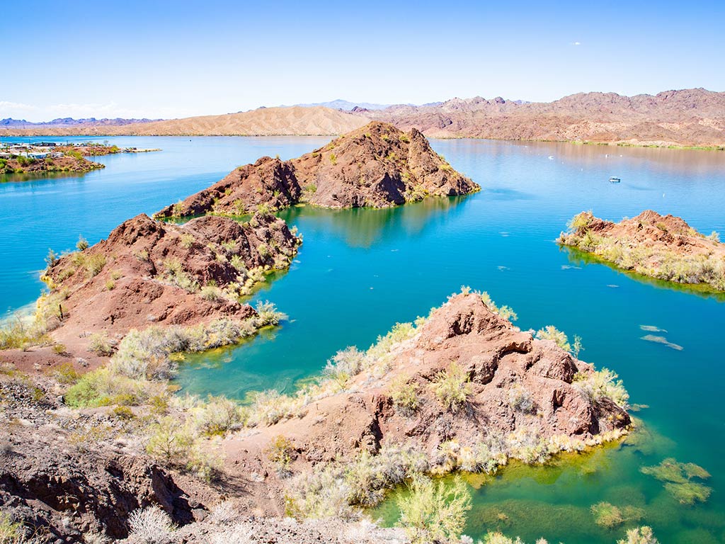 Rocky islands and desert vegetation scattered across a bright blue Lake Havasu in California, all set against majestic mountains and a clear sky.