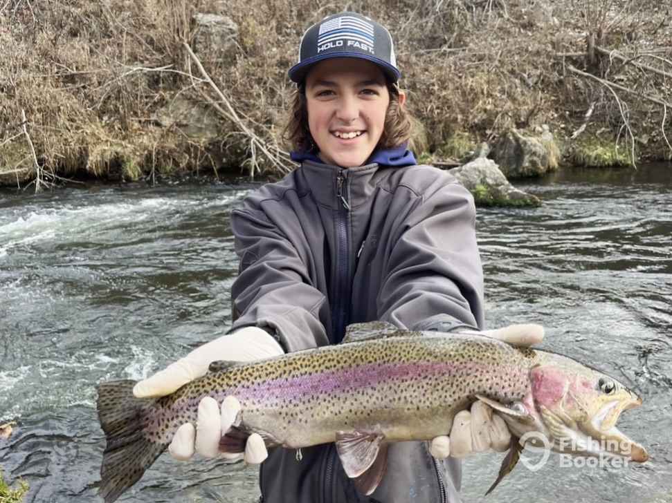 A young boy with long hair holds out a Rainbow Trout in front of her on a grey day on the White River in Arkansas.