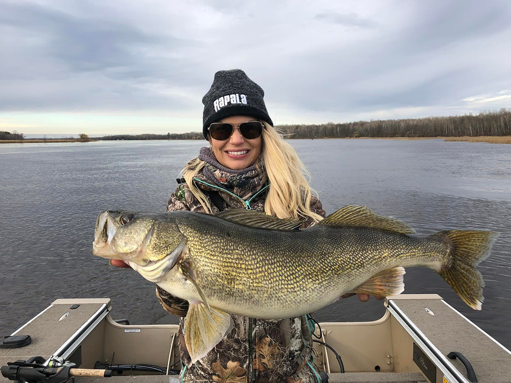 A woman on a boat in Minnesota holding a large Walleye under cloudy skies.