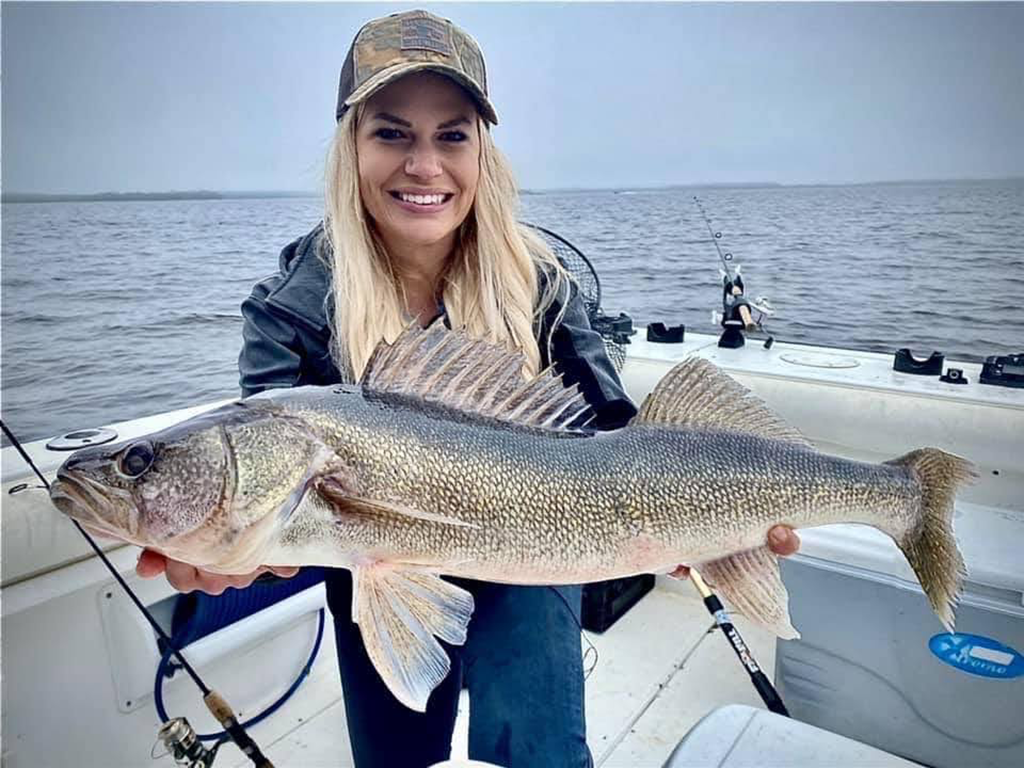 A woman in a baseball cap holding a large Walleye on a boat on Lake of the Woods in Minnesota on a cloudy day.