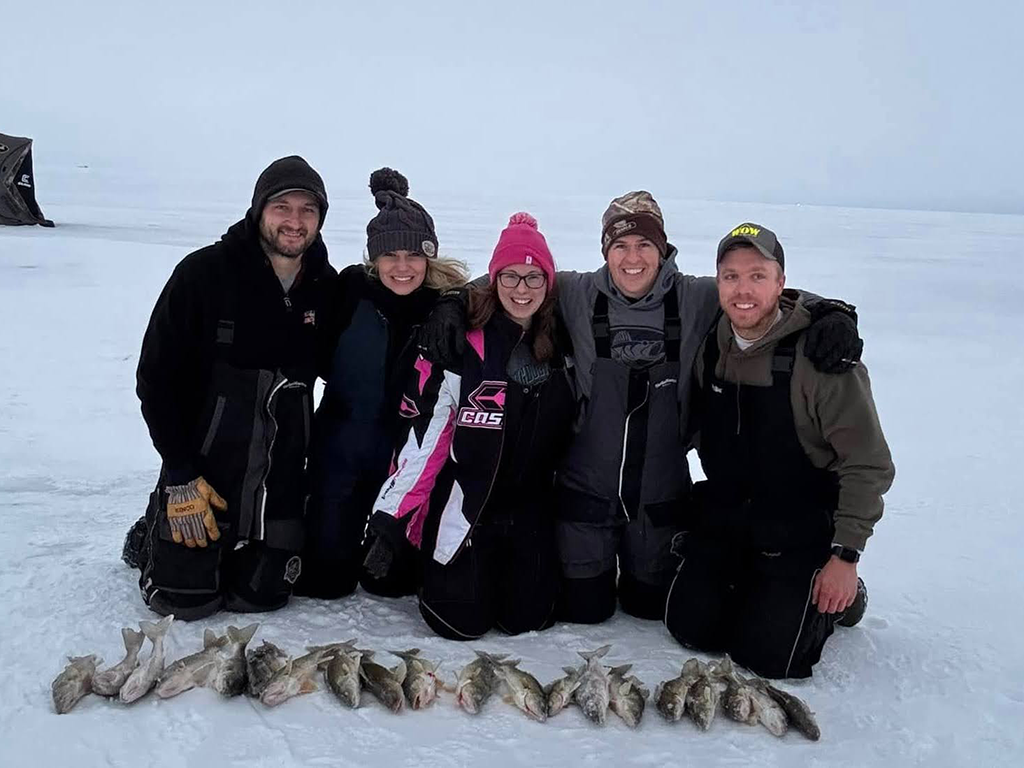 A family kneeling on the ice on a frozen lake in Minnesota in winter behind their spread of Walleye caught while ice fishing.