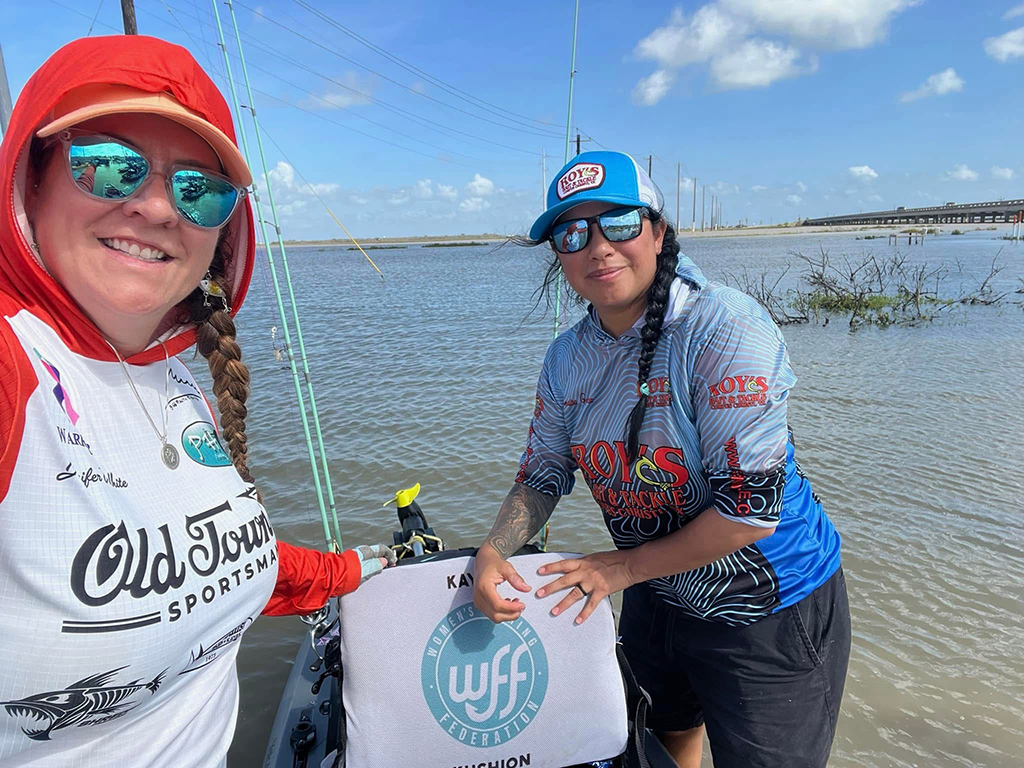 A woman taking a selfie with a friend while on a biat with a seat visible, sporting the WFF logo on a clear day.