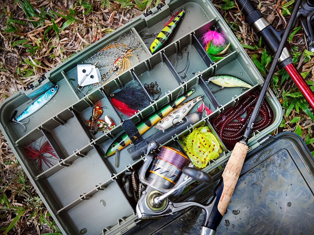 A view from above of a tackle box featuring jerkbaits and soft plastics, with a rod and reel lying on top of the box.