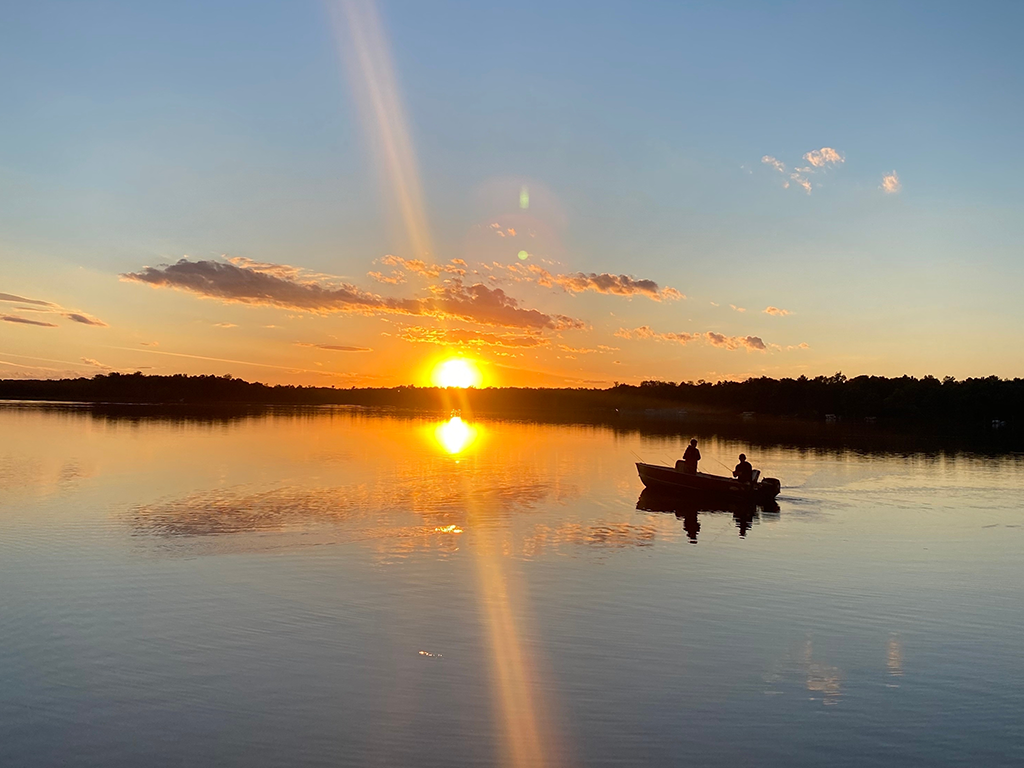 A view across a calm lake in Minnesota at sunset with a lone boat on the water fishing.