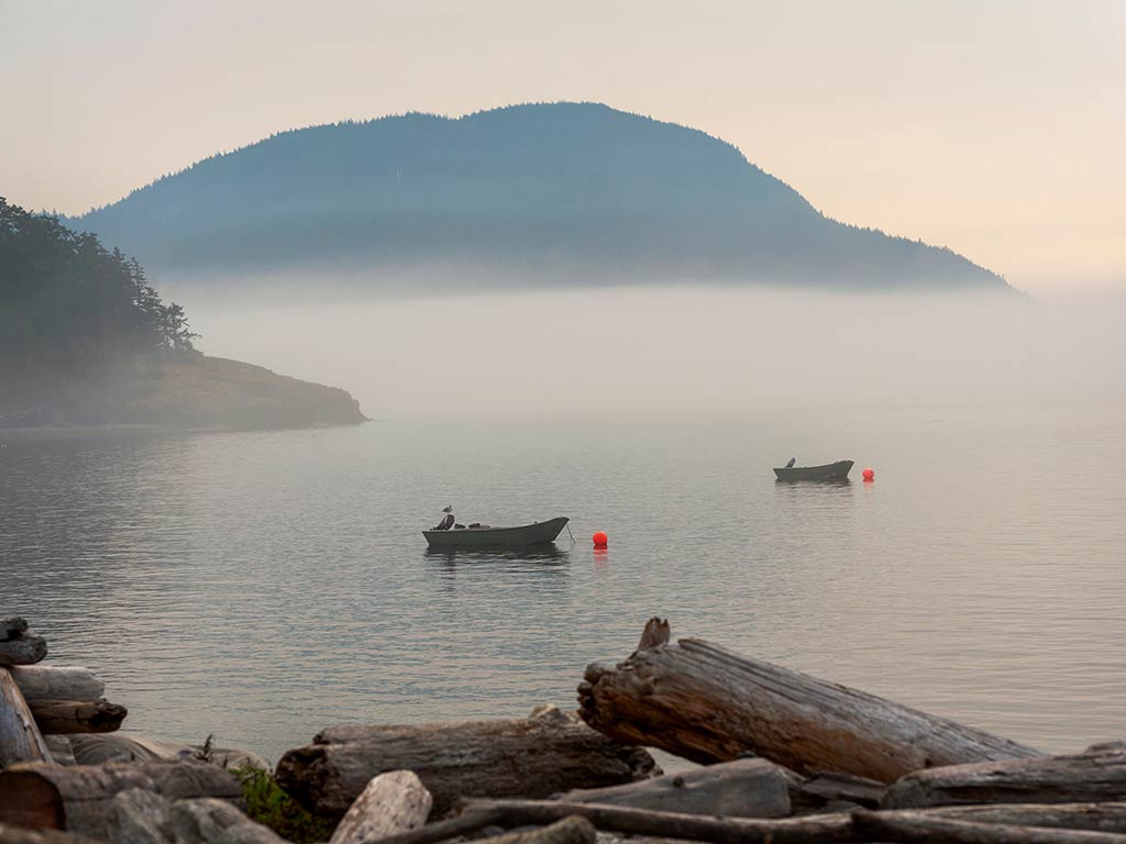A view across the water near the San Juan Islands on a misty morning, with a couple of boats visible on the water.