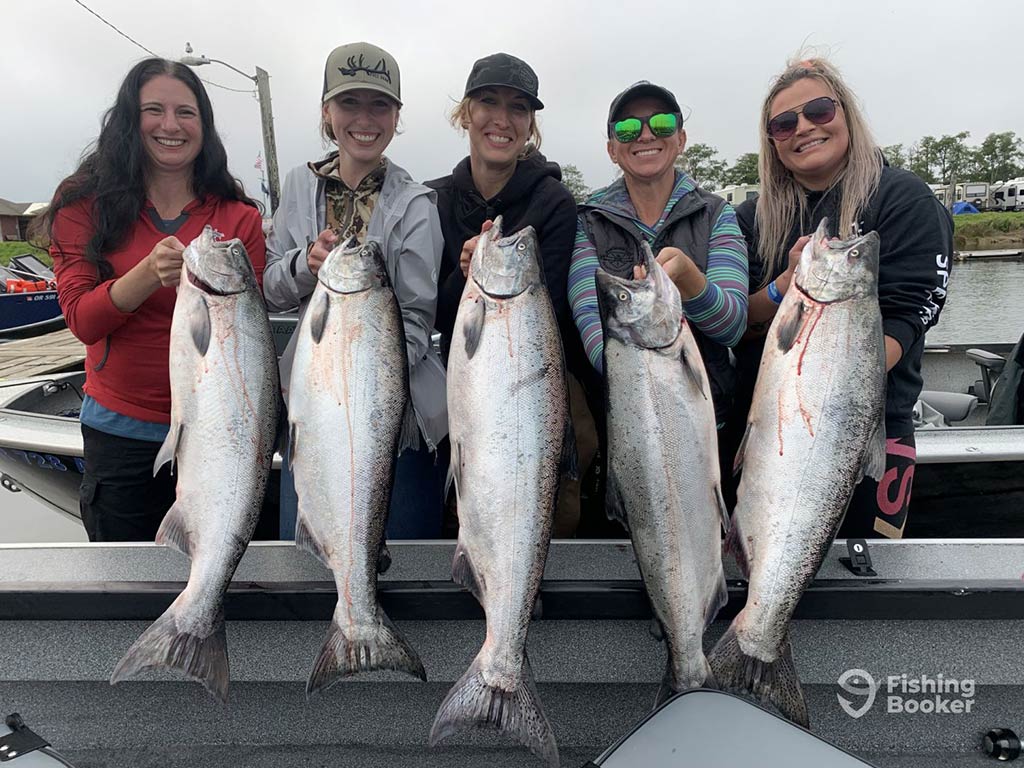 A group of anglers standing and smiling with their catch of numerous Salmon near the San Juan Islands in Washington state ona cloudy day.