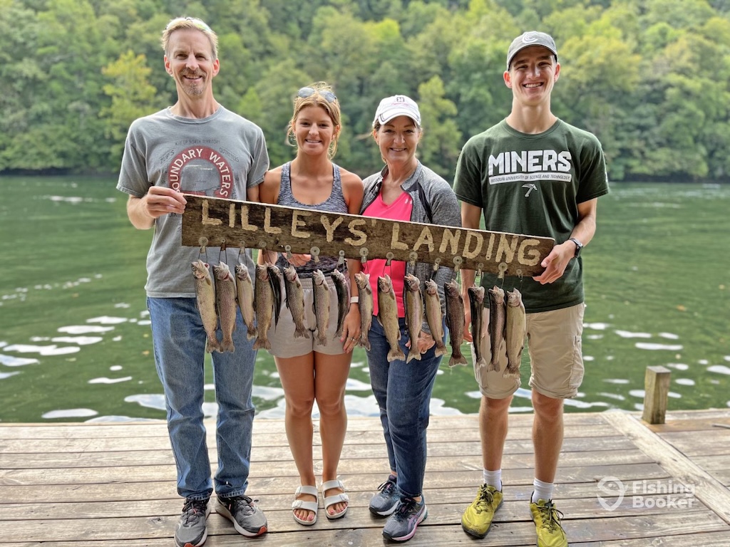 Four people stand on a dock holding a "Lilleys Landing" sign with several Trout, highlighting Trout Fishing in Missouri; water and trees complete the scene.