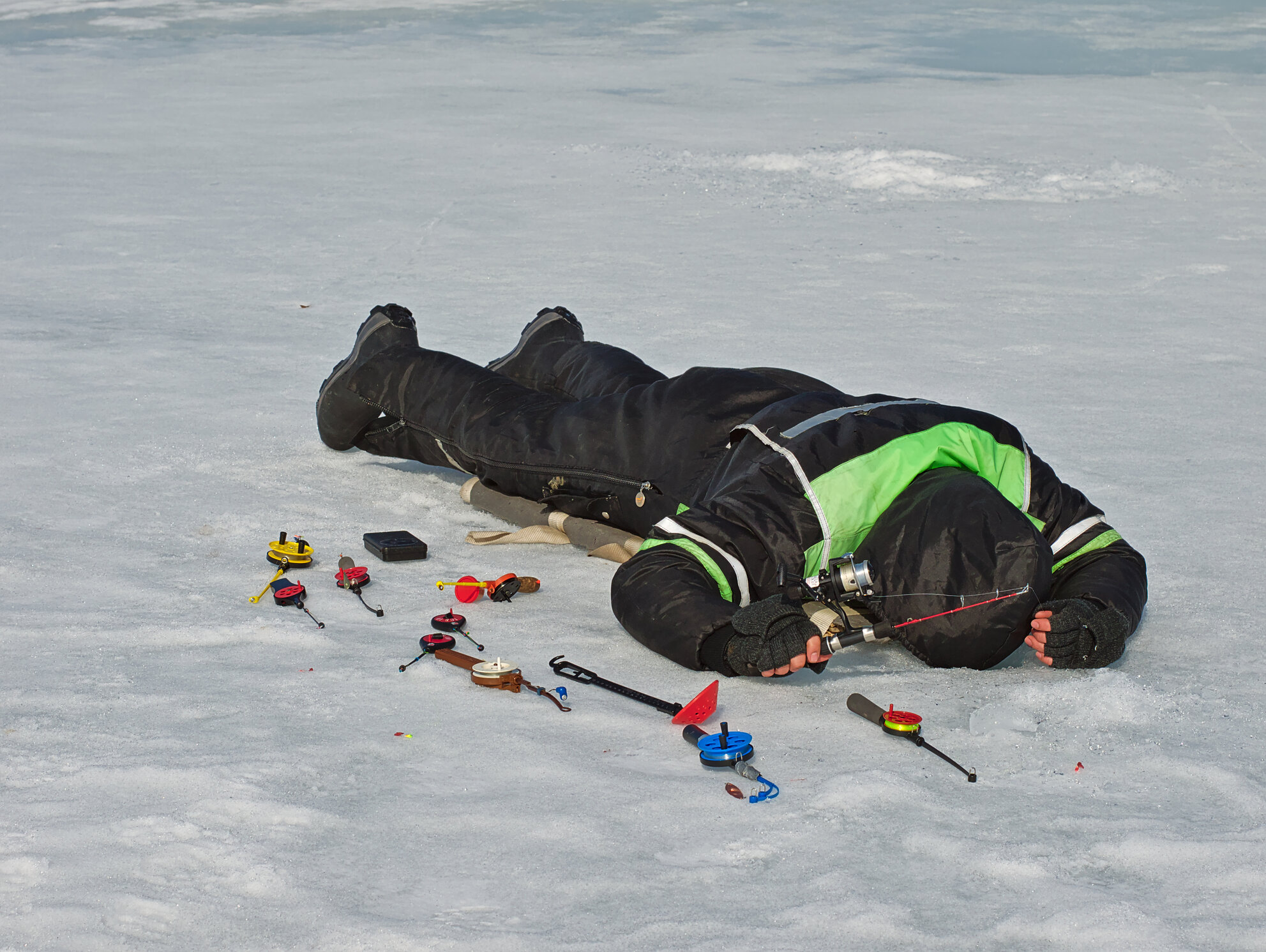 Ein Eisangler in Finnland liegt auf dem Bauch, um die Fische unter dem Eis zu sehen.