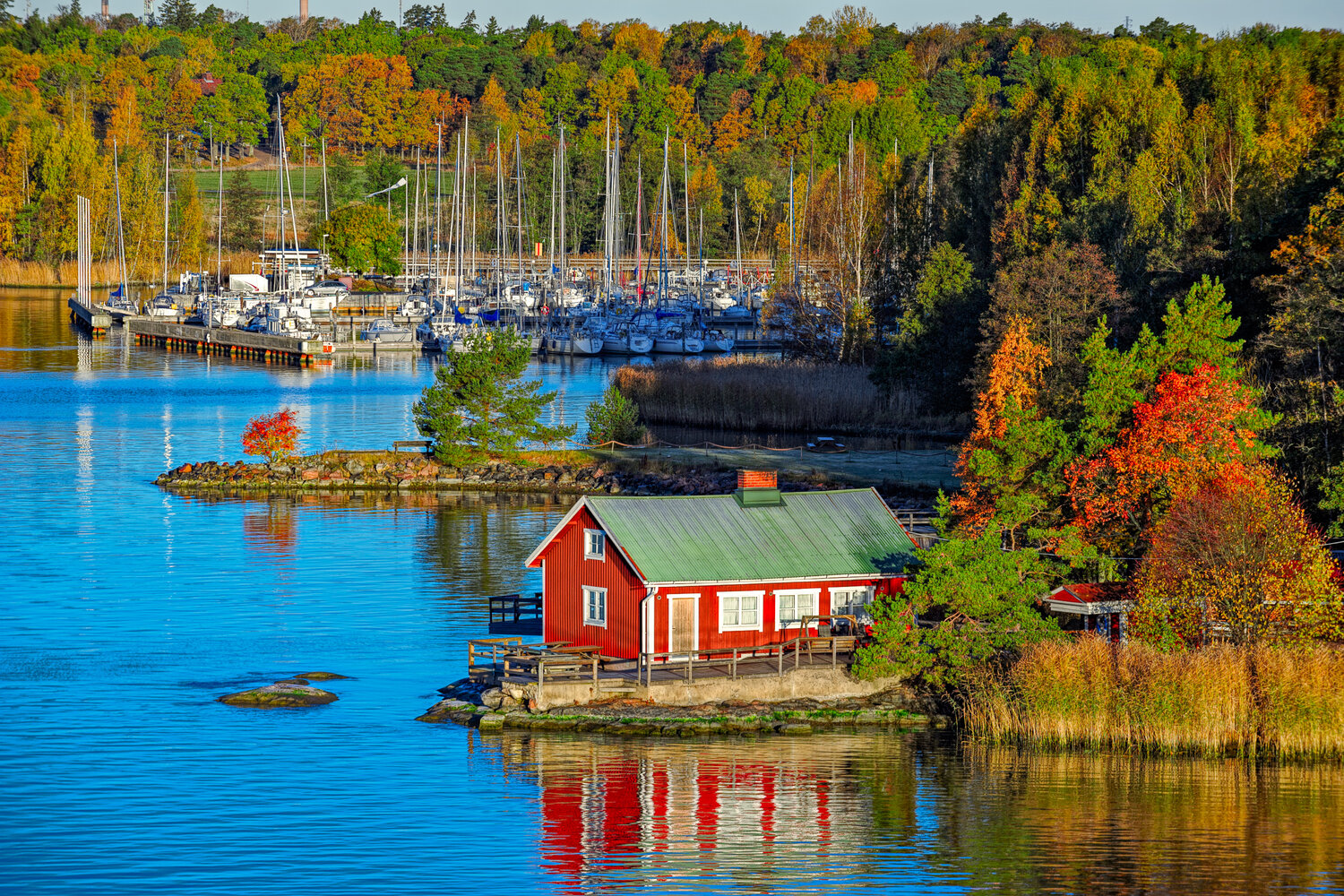 Ein rotes Haus auf einer der gro&szlig;en Inseln vor Turku mit einem Yachthafen im Hintergrund.